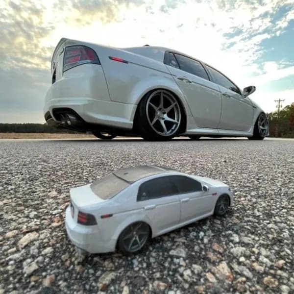 A low-angle shot of a 3D printed sedan replica with the full-size car behind it