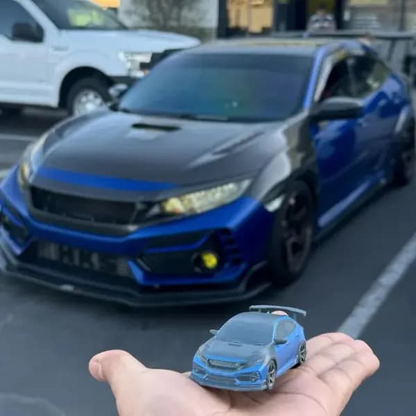 A blue custom 3D printed hatchback replica held beside the real car