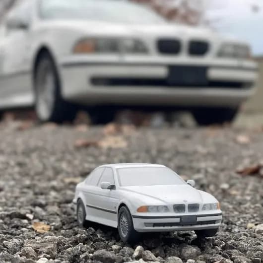 A white 3D printed sedan replica photographed on gravel in front of the real car