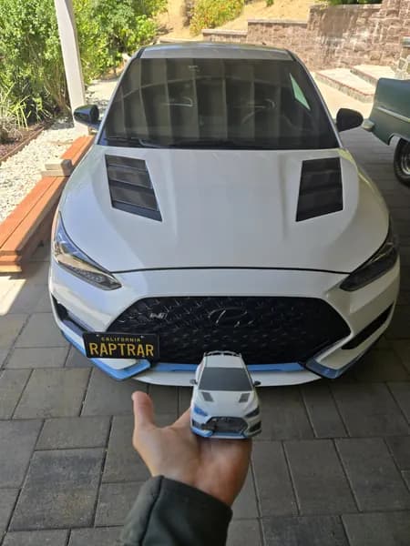 A 3D printed Mustang replica held in front of the full-size car it copies