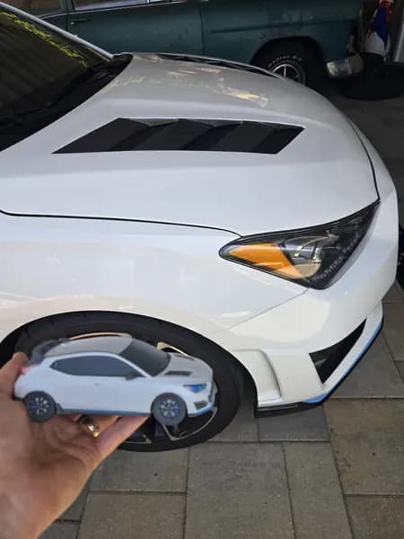 A 3D printed Hyundai Veloster N replica held in front of the real car