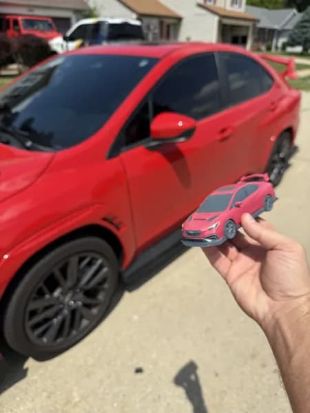 A custom 3D printed Subaru replica held up beside the full-size car for scale