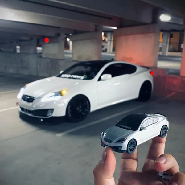A hand holding a white 3D printed coupe replica in front of the matching real car