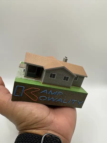 A custom 3D printed house replica held in one hand, showing roof and siding detail