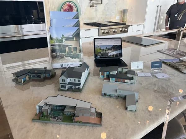 A set of custom 3D printed house models laid out beside the renders they were built from