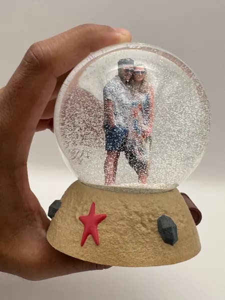 A hand holding a custom snow globe with a sculpted sand base and starfish