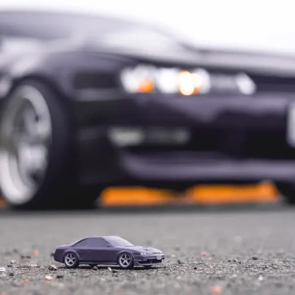 A close macro of a purple 3D printed sports car replica beside the real car