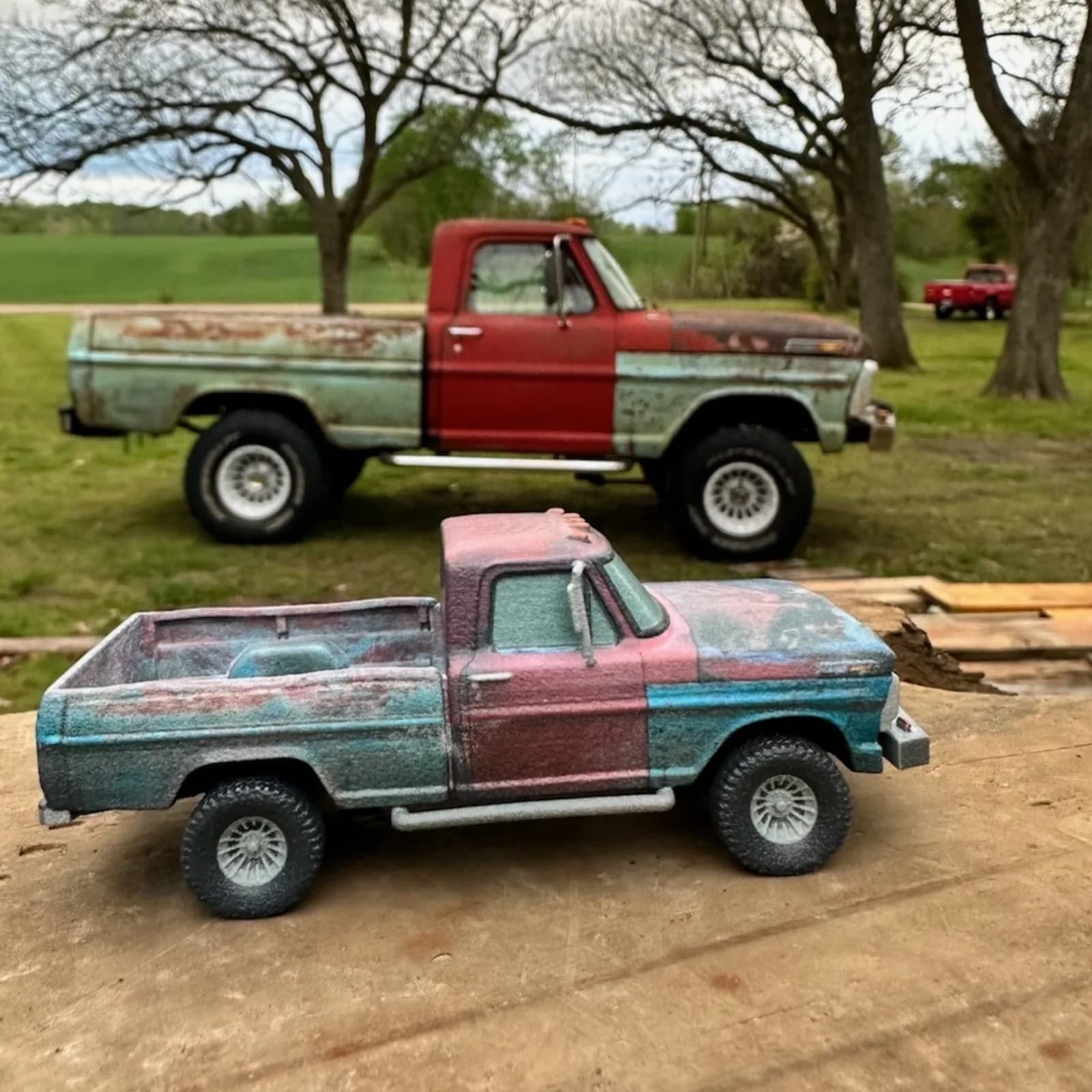 A weathered two-tone 3D printed pickup replica in front of the full-size truck