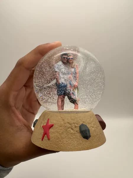 A custom 3D printed snow globe containing a couple on a hand-sculpted sand base with a starfish