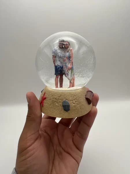 A custom 3D printed snow globe containing a couple on a hand-sculpted sand base with a starfish