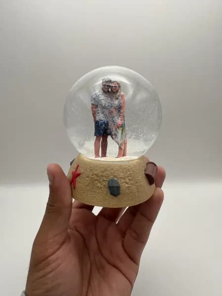 A custom 3D printed snow globe containing a couple on a hand-sculpted sand base with a starfish