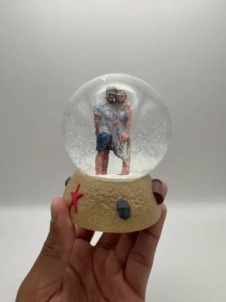 A custom 3D printed snow globe containing a couple on a hand-sculpted sand base with a starfish