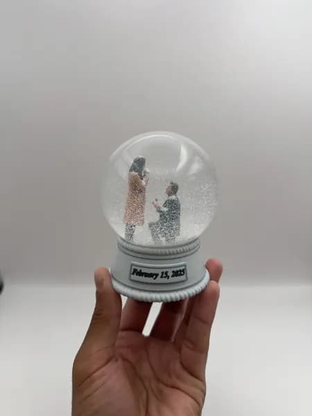 A custom 3D printed snow globe containing a proposal scene, with the date on the base