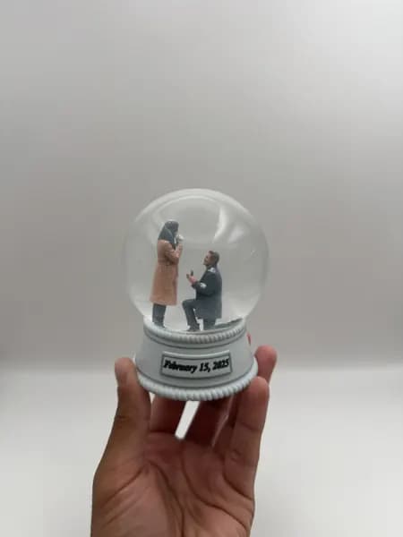 A custom 3D printed snow globe containing a proposal scene, with the date on the base