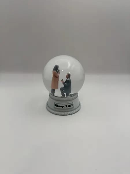 A custom 3D printed snow globe containing a proposal scene, with the date on the base